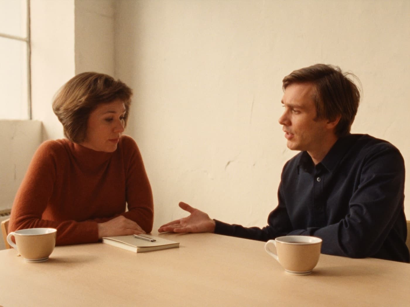 A coach listening to a client across a table in a sunlit room