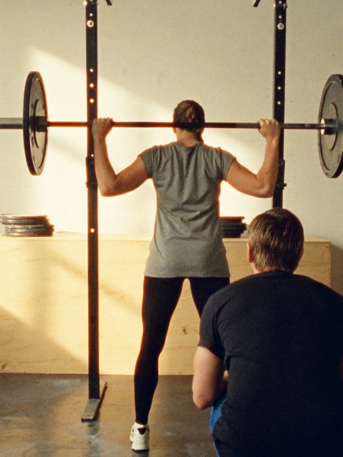 A personal trainer spotting a client at a squat rack in a bright gym