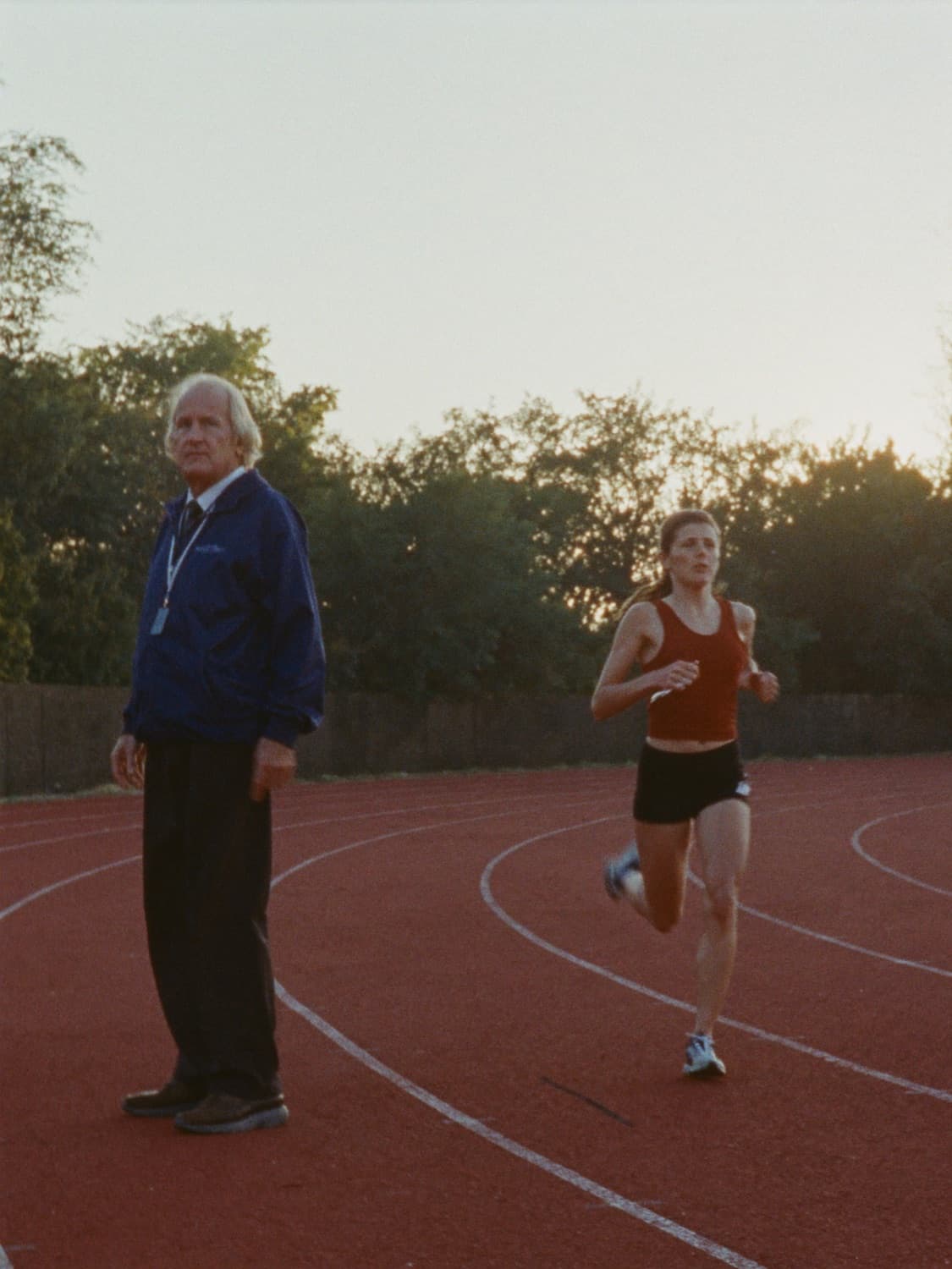 A running coach watching a runner come round the bend of a track at sunrise