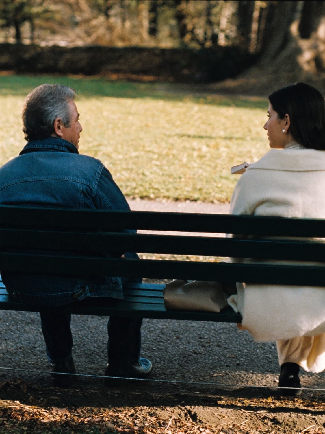 Two people talking on a park bench in autumn light